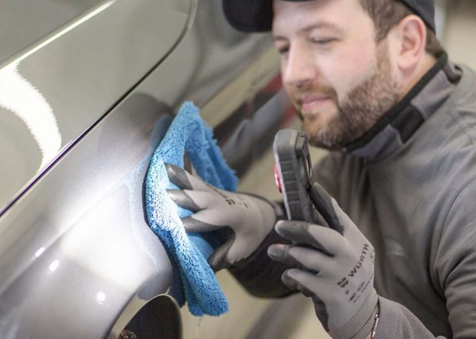 Person untersucht Lack am Fahrzeug